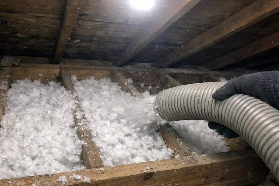 A blower hose filling an attic joist bay with fresh loose-fill insulation