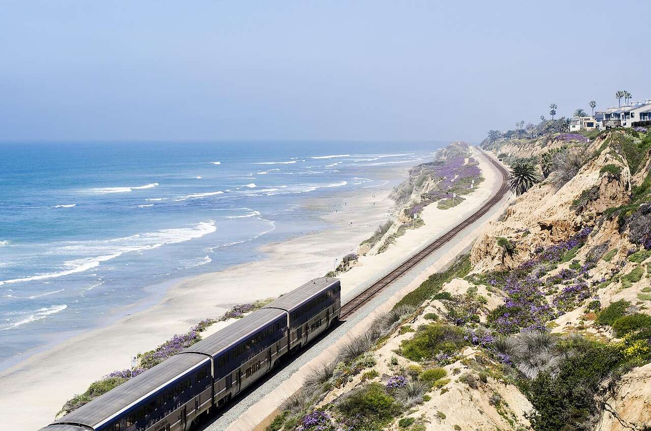 A passenger train running along the coastal bluff at Del Mar above the beach