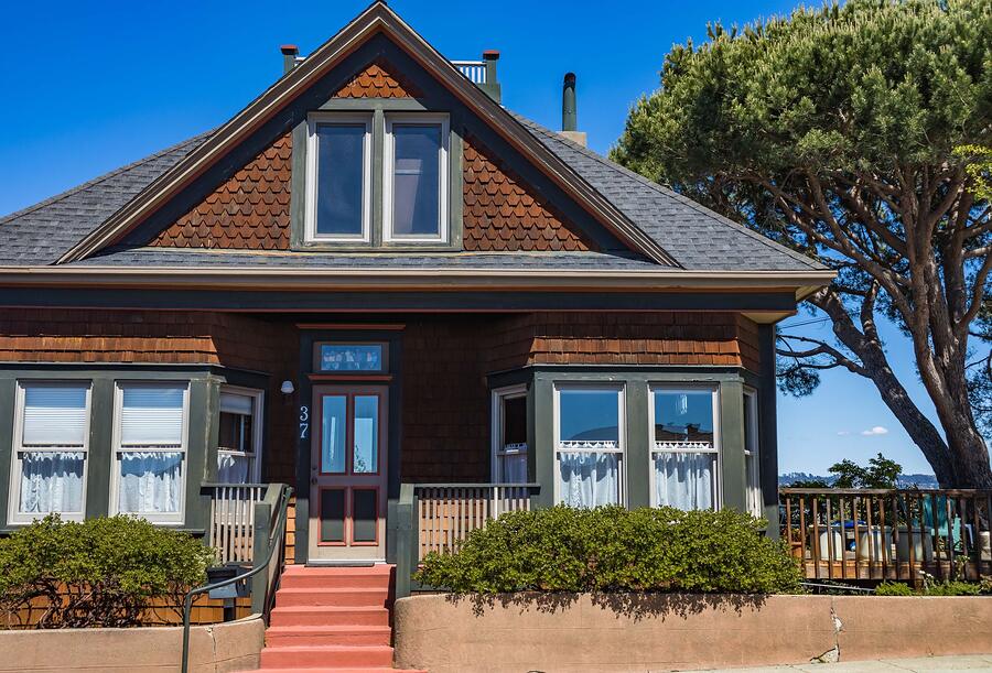An older wood-frame house with a deep porch and a mature tree against the roofline