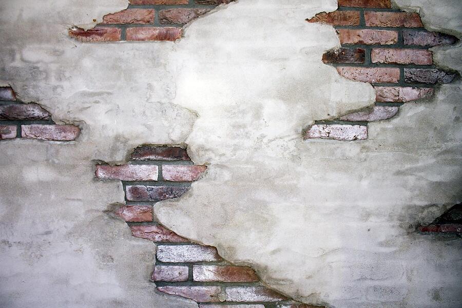 An old stucco wall with the render crumbled away to expose the brick beneath