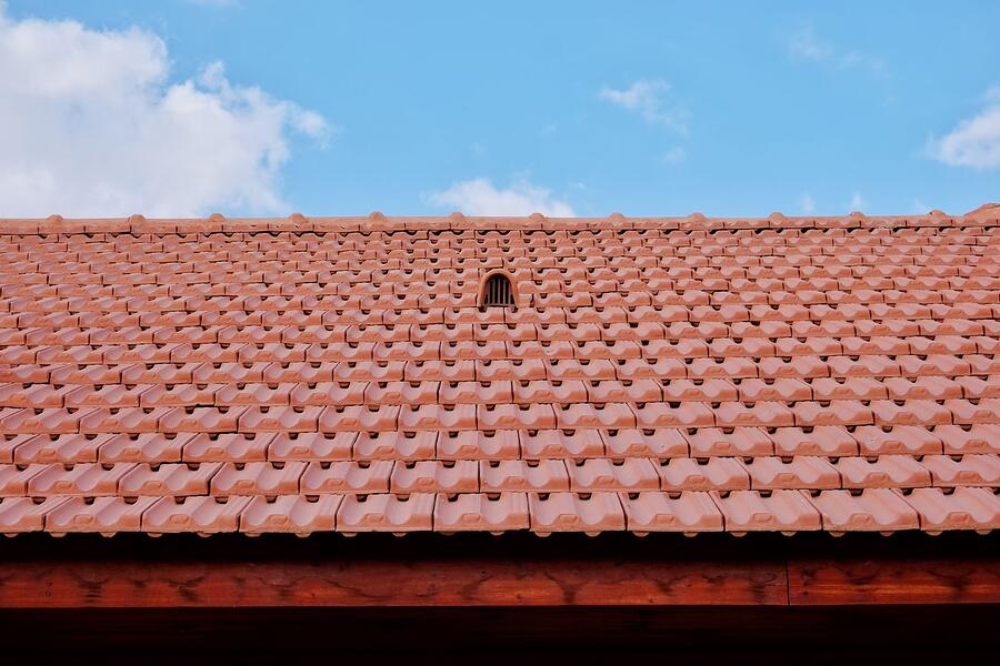 A red S-tile roof with a vent, seen against a clear sky