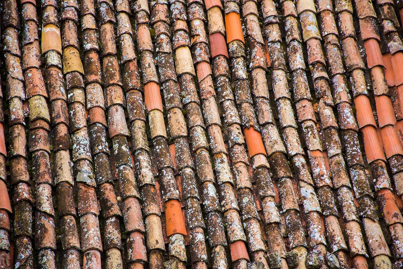 Weathered clay barrel tiles on a roof, the eave course of which is closed with a metal bird stop