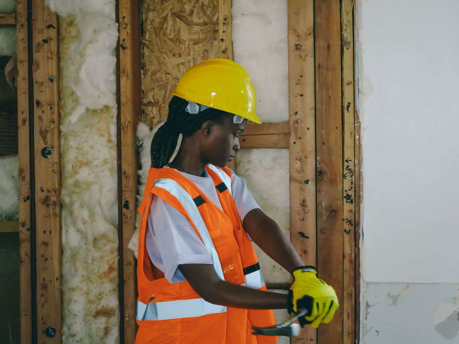 A worker in a reflective vest and hard hat fitting insulation into open framing